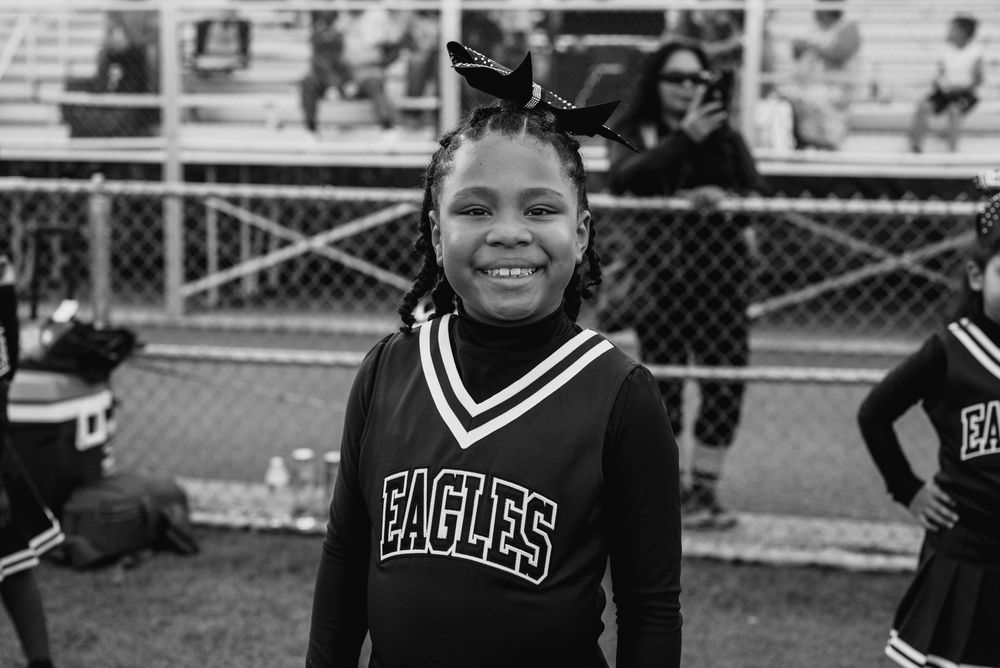 Smiling young Eagles cheerleader in black and white uniform at outdoor sports event.