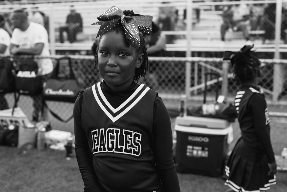 Young girl in Eagles cheerleader uniform standing near bleachers at football game, black and white.