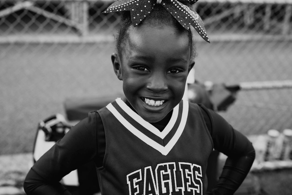 Happy young girl in Eagles cheerleader uniform smiles brightly with polka dot bow in hair.
