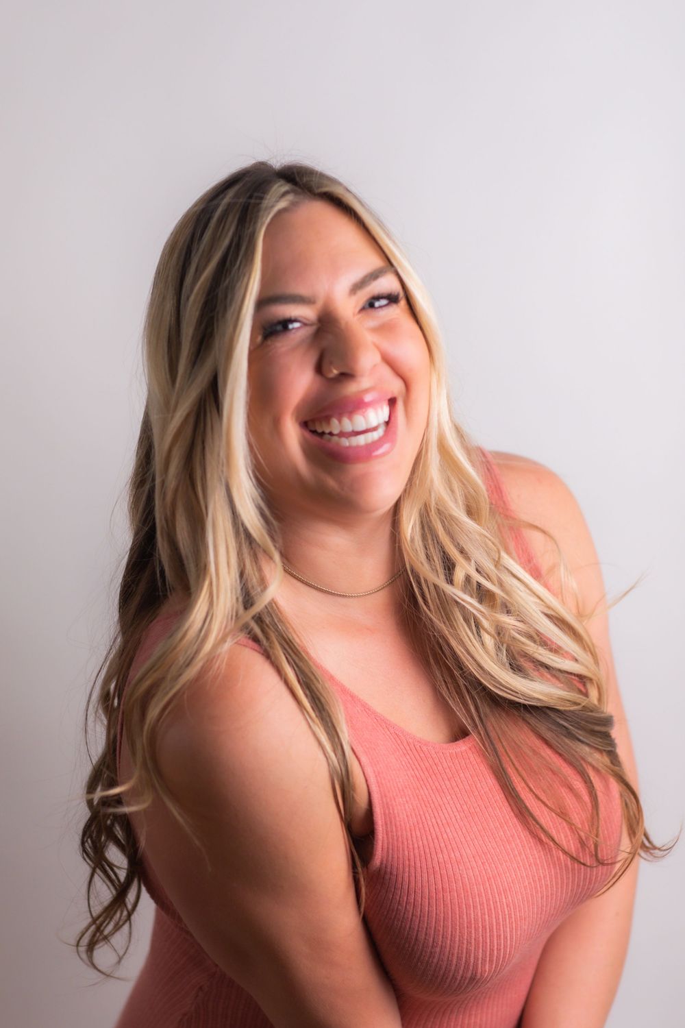 Cheerful blonde woman in pink ribbed top laughs naturally during a bright professional portrait session.