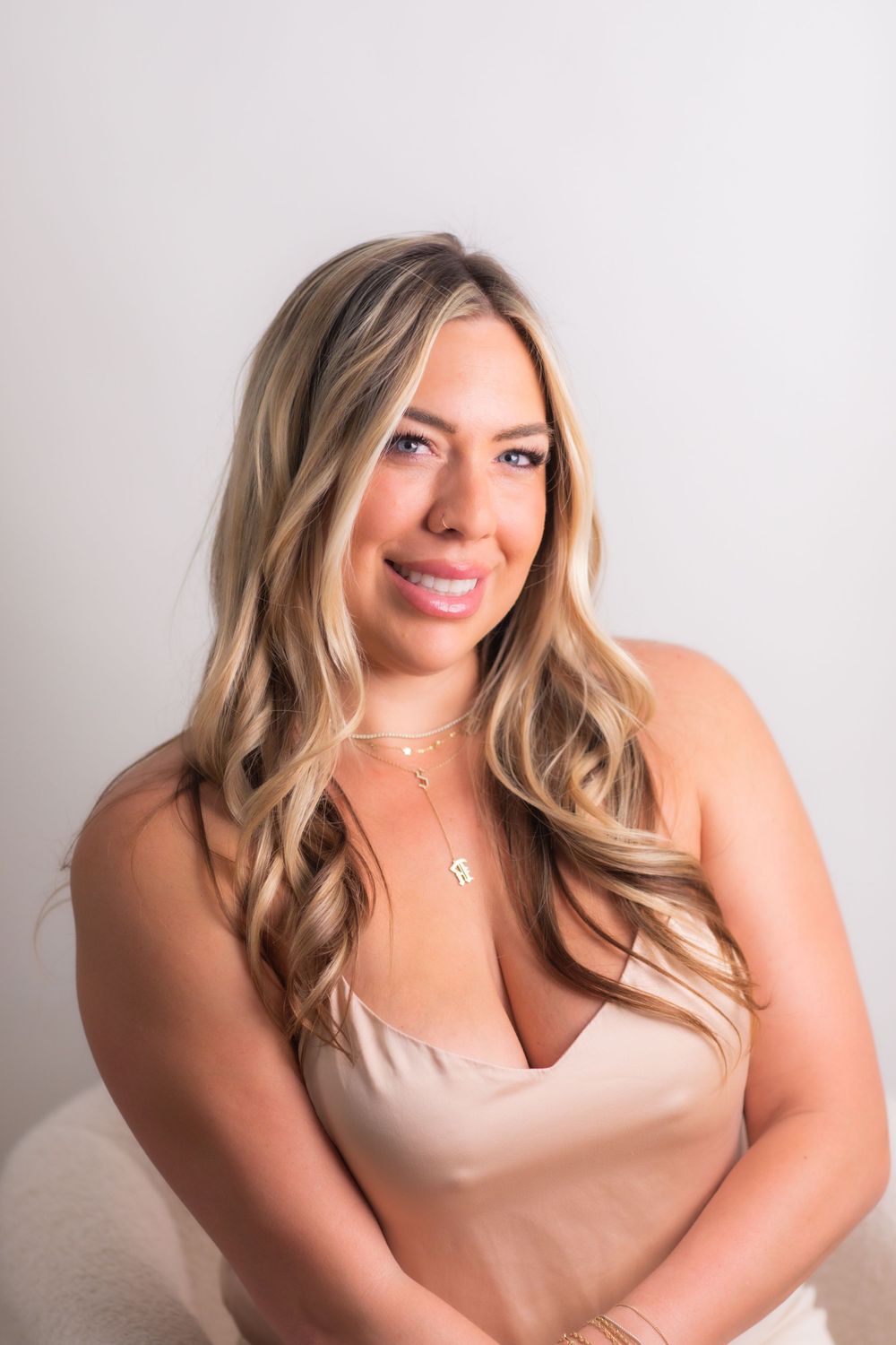 Smiling blonde woman in beige satin top with silver necklace poses for a professional portrait photo.