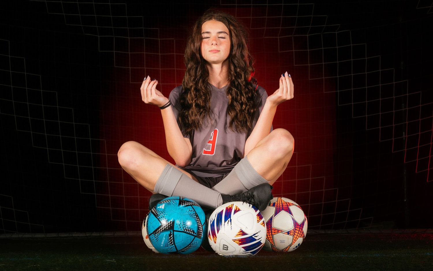 Parkland girls soccer player Media Day seated pose with balls and dramatic lighting, by Deanna Fox, SportsFox Photography, Hershey PA