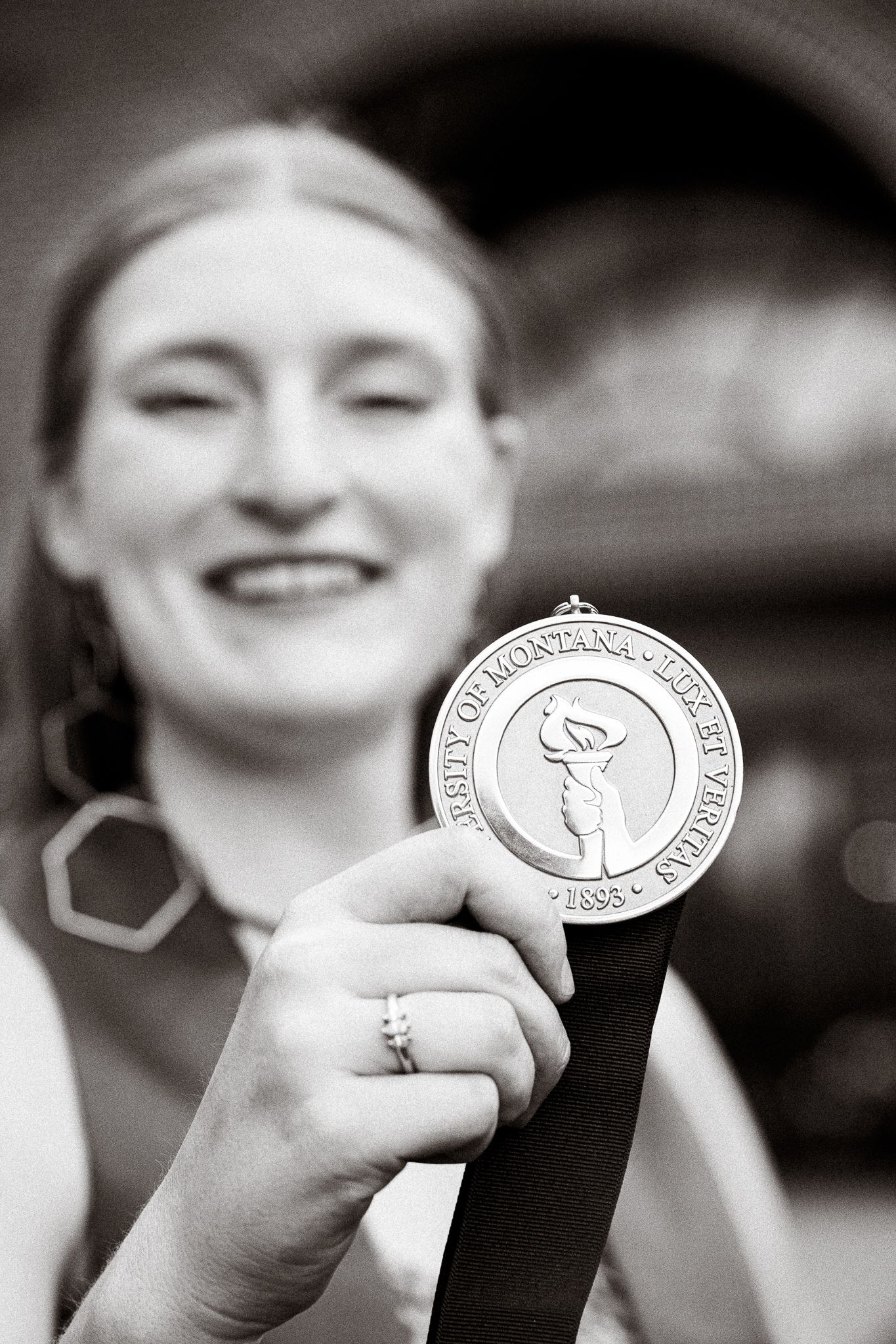 Smiling woman proudly holds a University of Montana medal on a ribbon in a black and white photo.