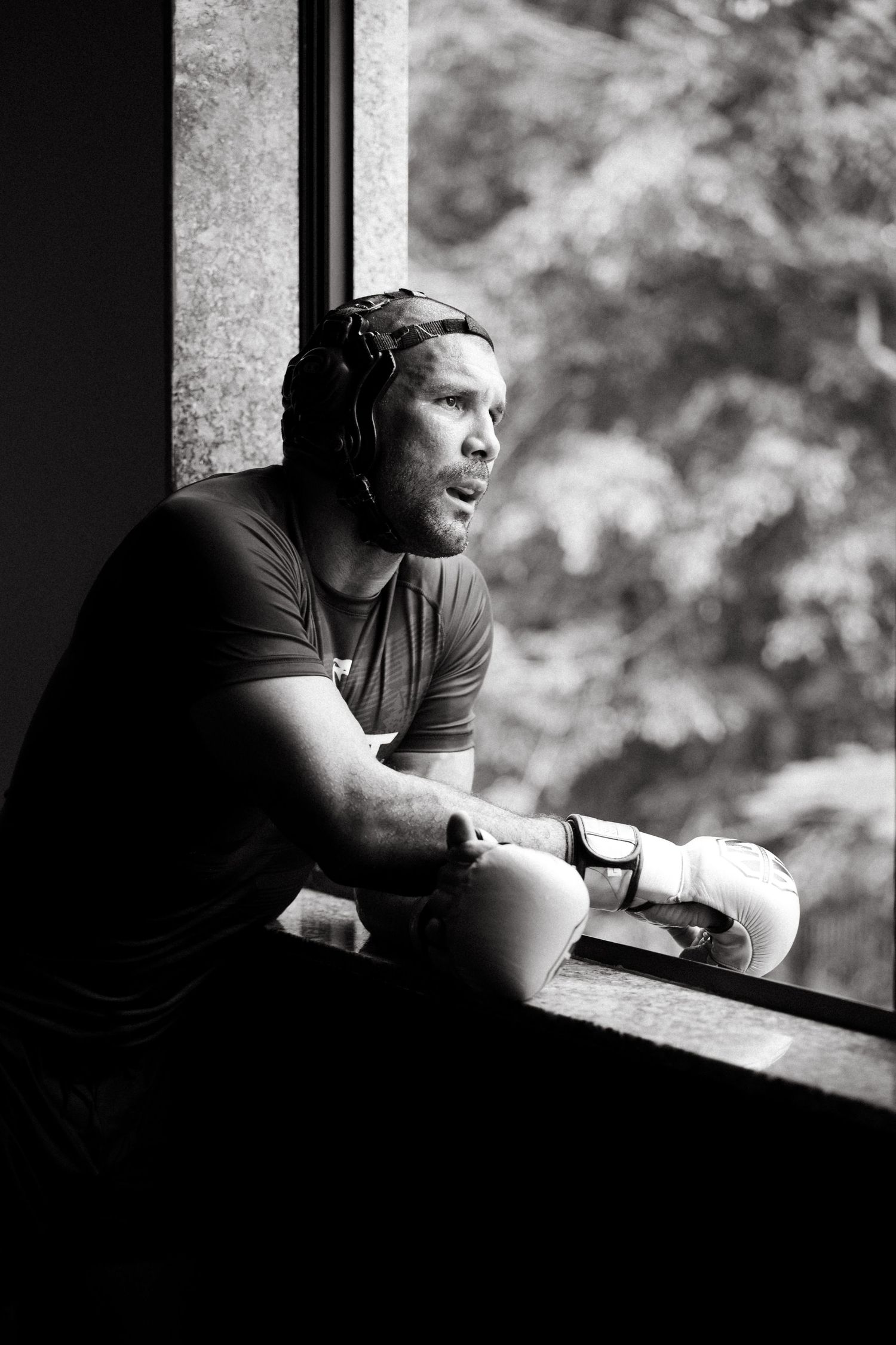 Black and white photo of Rodolfo Vieira in boxing gloves sitting by a window during training.