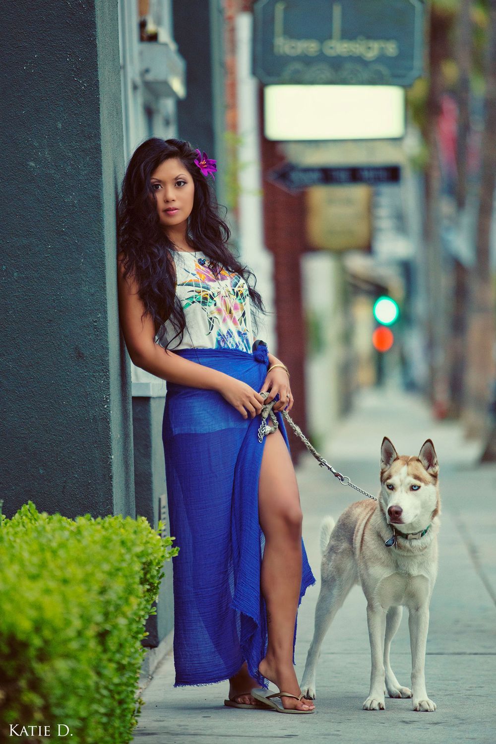 Brunette woman in blue maxi skirt holds a Husky dog leash on a city sidewalk.