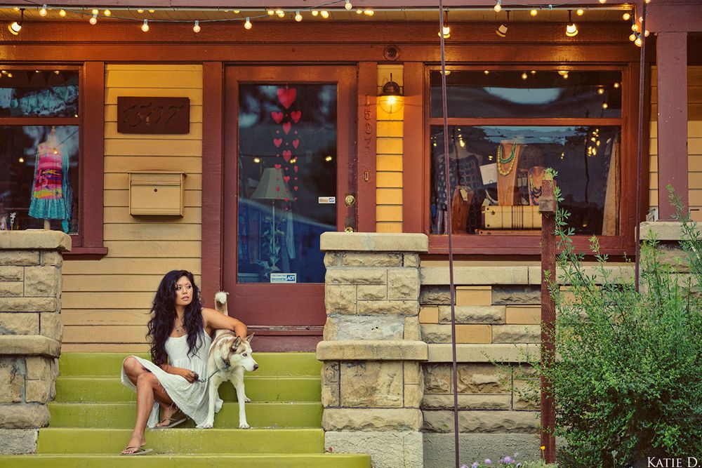 Woman sits on colorful shop steps with a Husky dog under warm string lights at dusk.