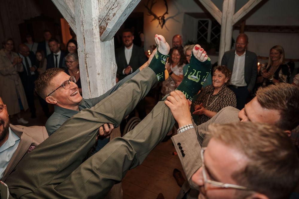 Lively crowd celebrating at a rustic indoor reception venue with wooden beams and warm lighting.