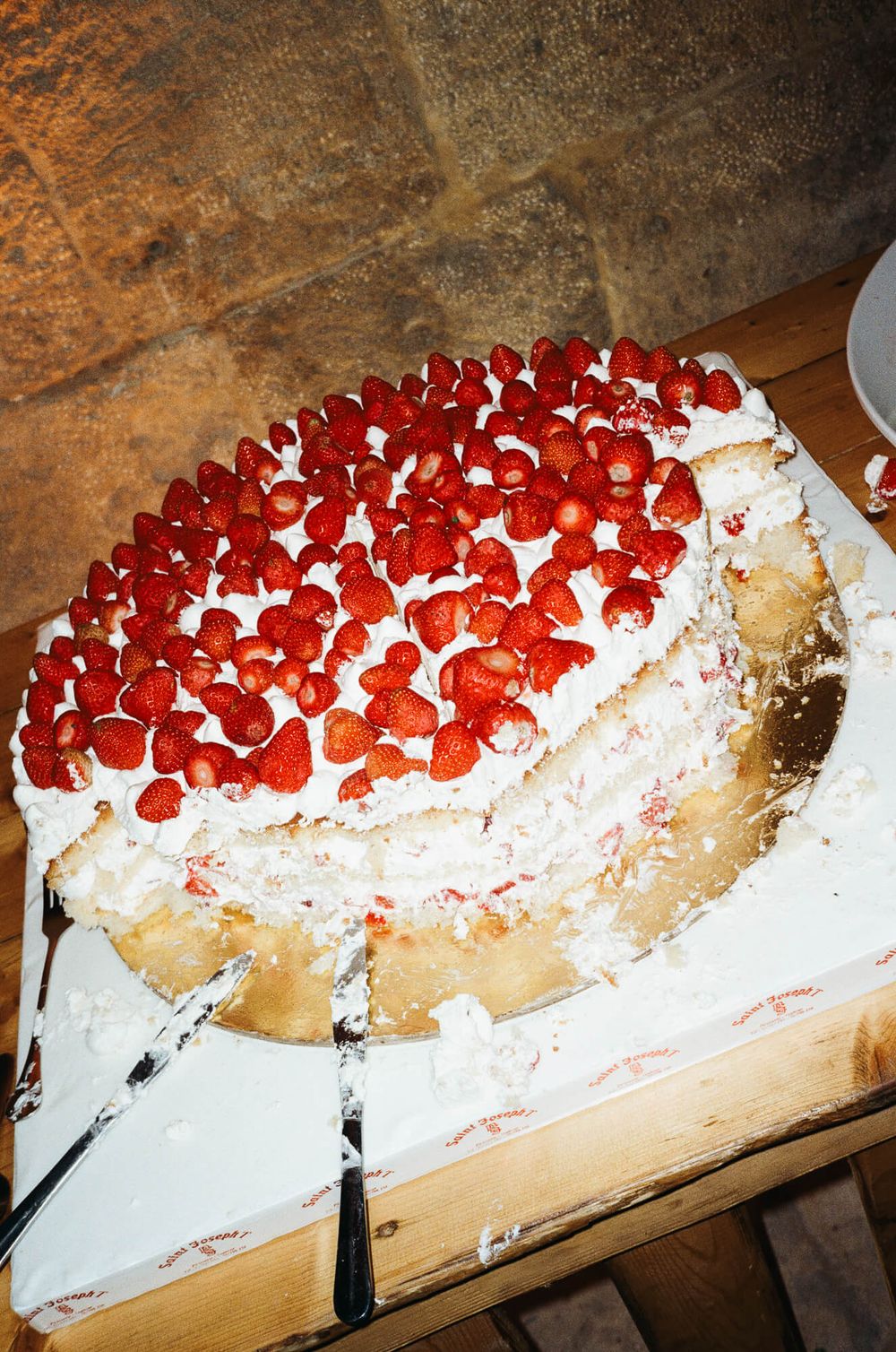 Partially sliced strawberry layer cake with whipped cream frosting and fresh strawberries on top, served on a gold board.