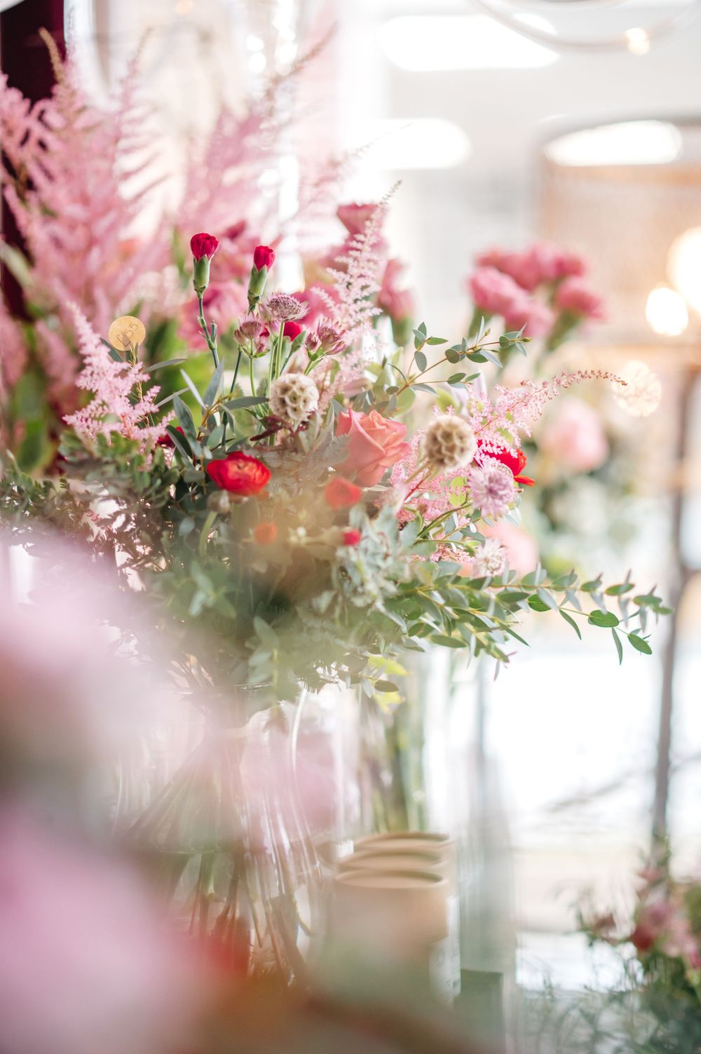 Elegant pink floral arrangement with carnations, astilbe, and eucalyptus in glass vases at a romantic wedding reception.