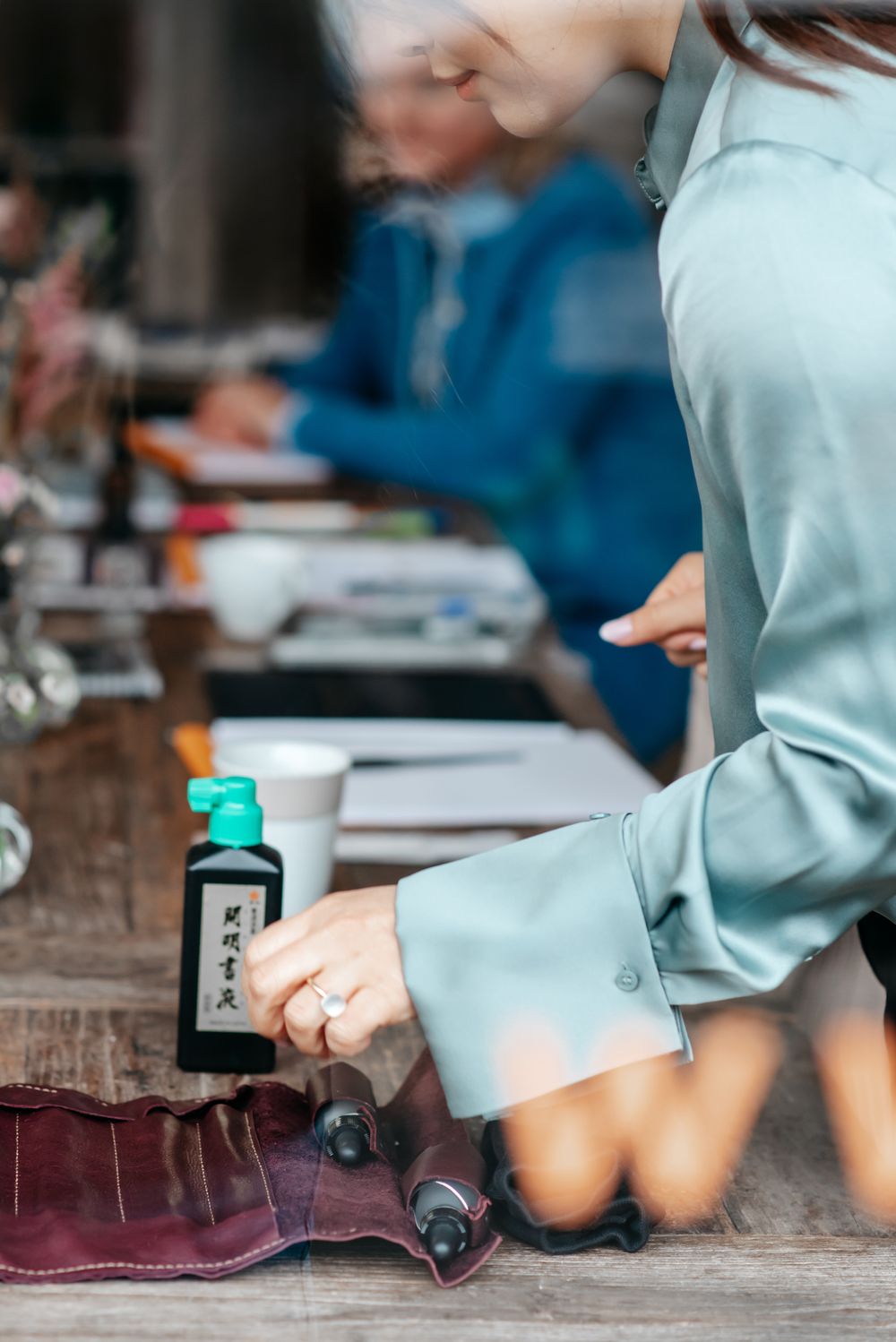 Woman in mint green blouse using Japanese ink at a wooden table during a calligraphy workshop.