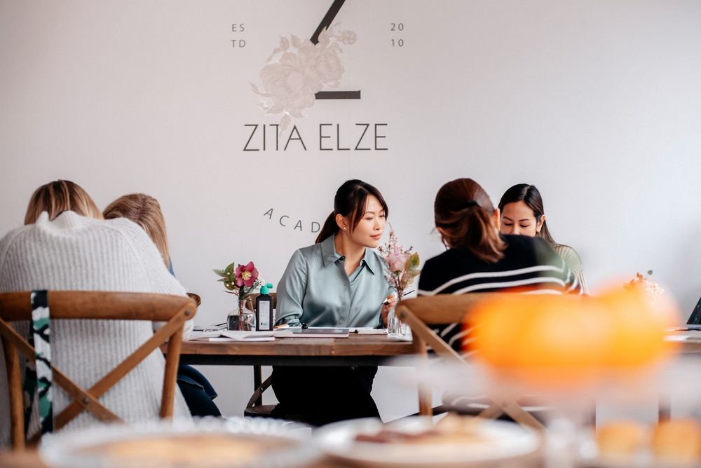 Women dining at Zita Elze Cafe, a bright minimalist restaurant with white walls and wooden chairs.