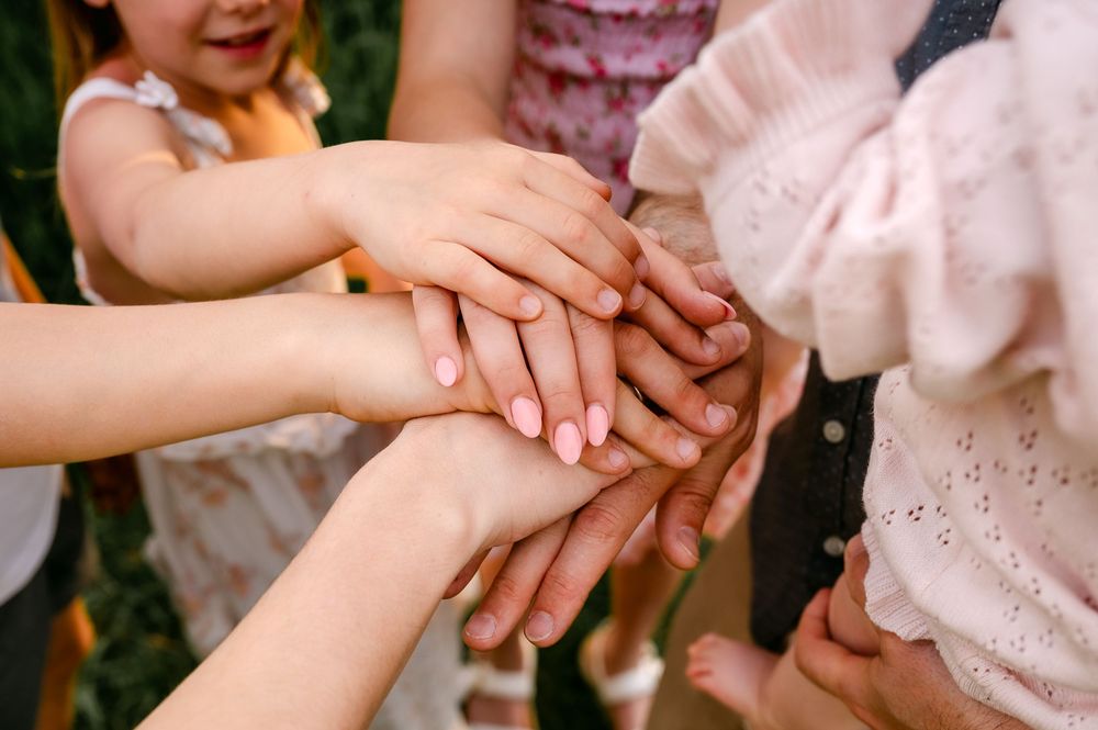 Children stacking hands together in a circle, symbolizing teamwork, friendship, and unity outdoors.