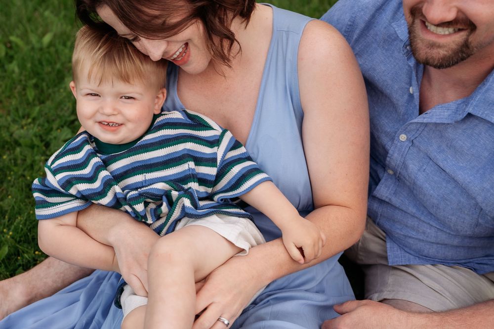 A happy family with a toddler boy in a striped shirt sitting outdoors on green grass.