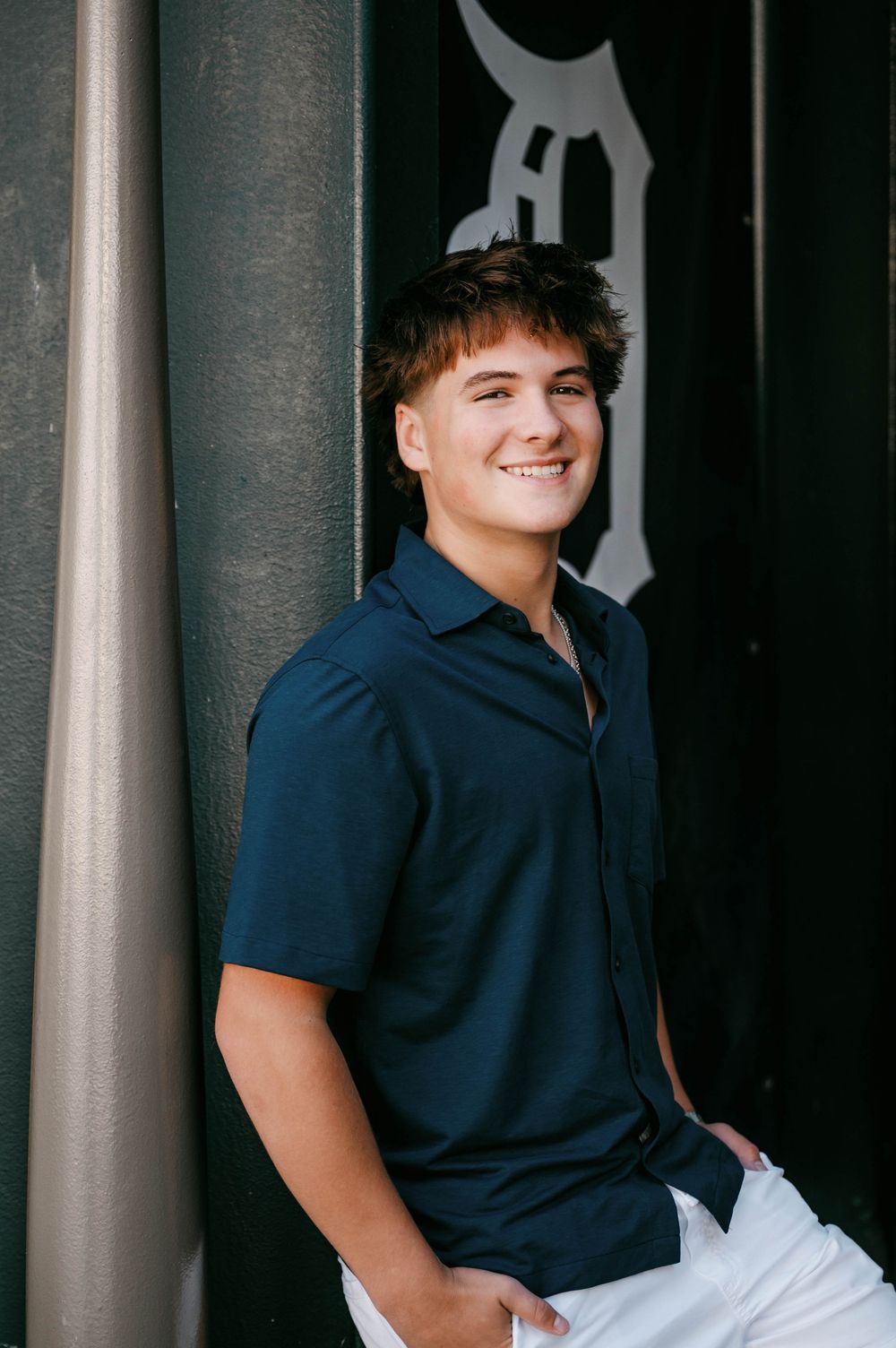 Smiling teenage boy in navy shirt and white pants leaning against a pillar at Comerica Park, Detroit Tigers stadium.