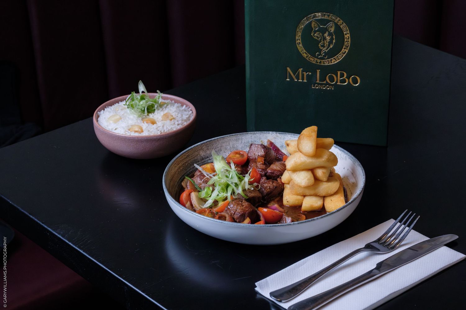 Mr LoBo restaurant dish featuring grilled meat, fresh salad, chunky chips, and a side of rice on a dark table.
