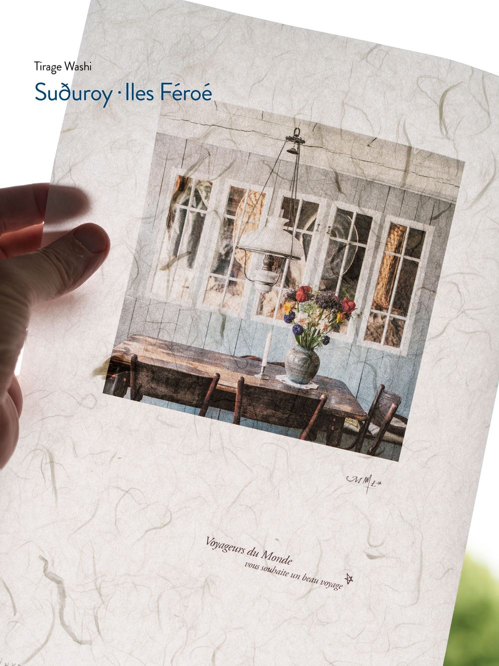 Hand holding a Washi print of Suðuroy Faroe Islands featuring a rustic dining room with flowers and candlelight.