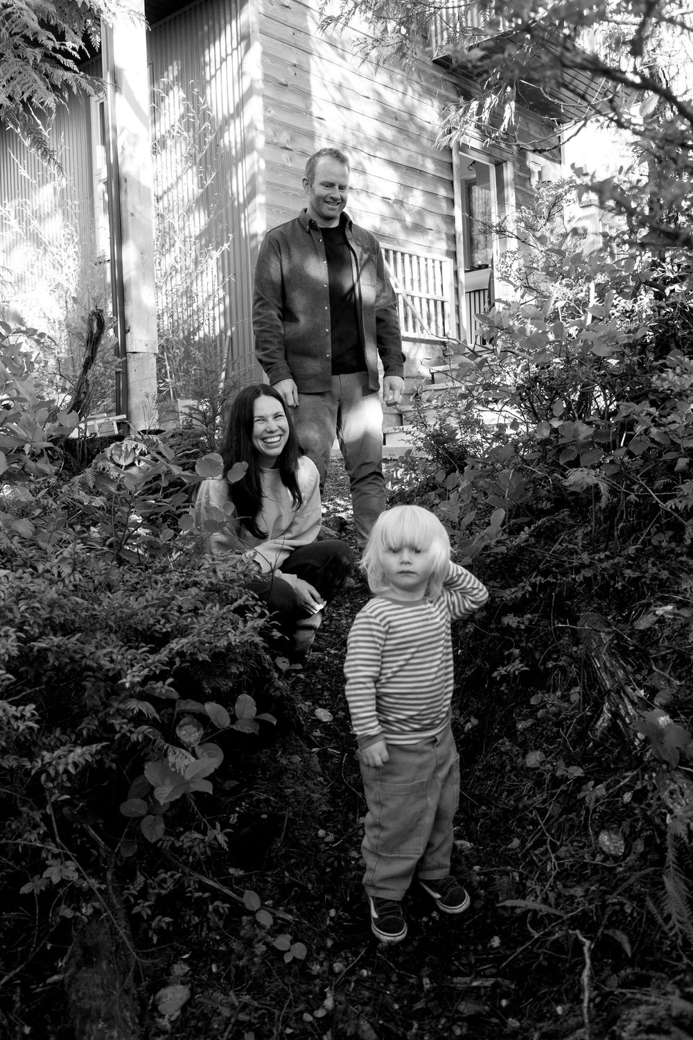 A black and white photo of a family with a toddler in a lush backyard garden.