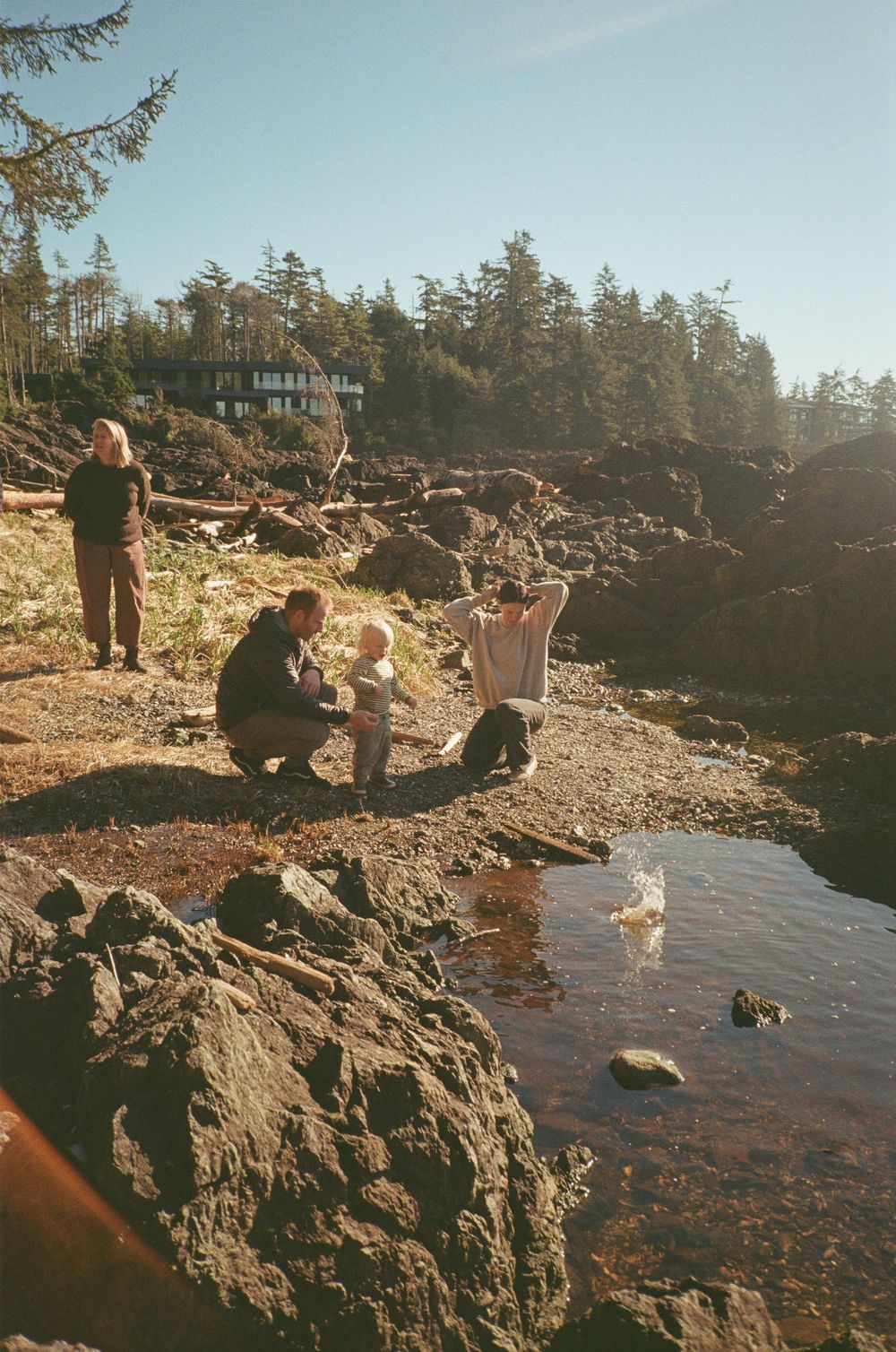 A family with a toddler explores a rocky coastal shoreline on a sunny clear day.