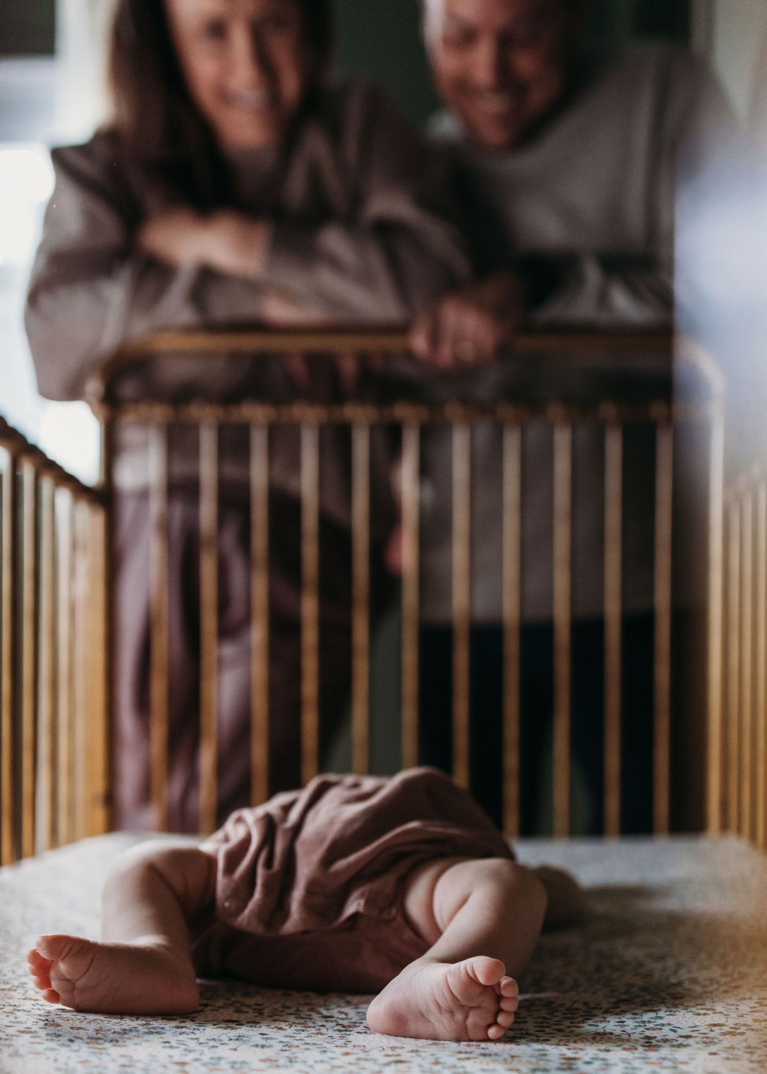 Grandparents lovingly gazing down at newborn baby lying in wooden crib, soft focus portrait.