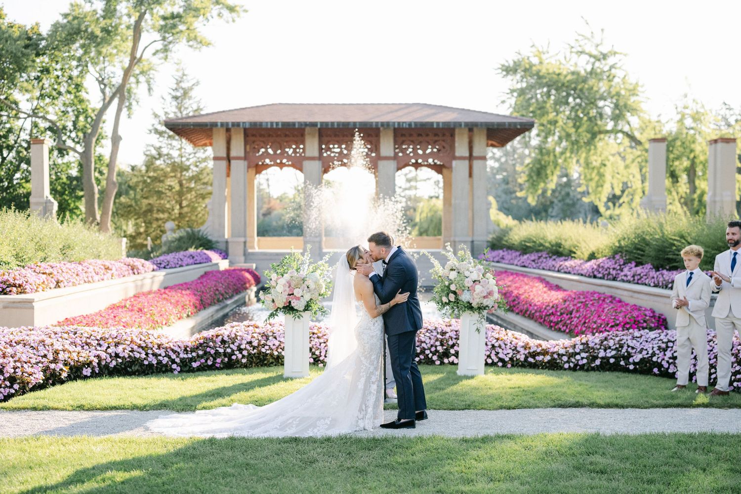 Armour House Wedding - Couple shares first kiss at outdoor wedding ceremony surrounded by colorful flower gardens.