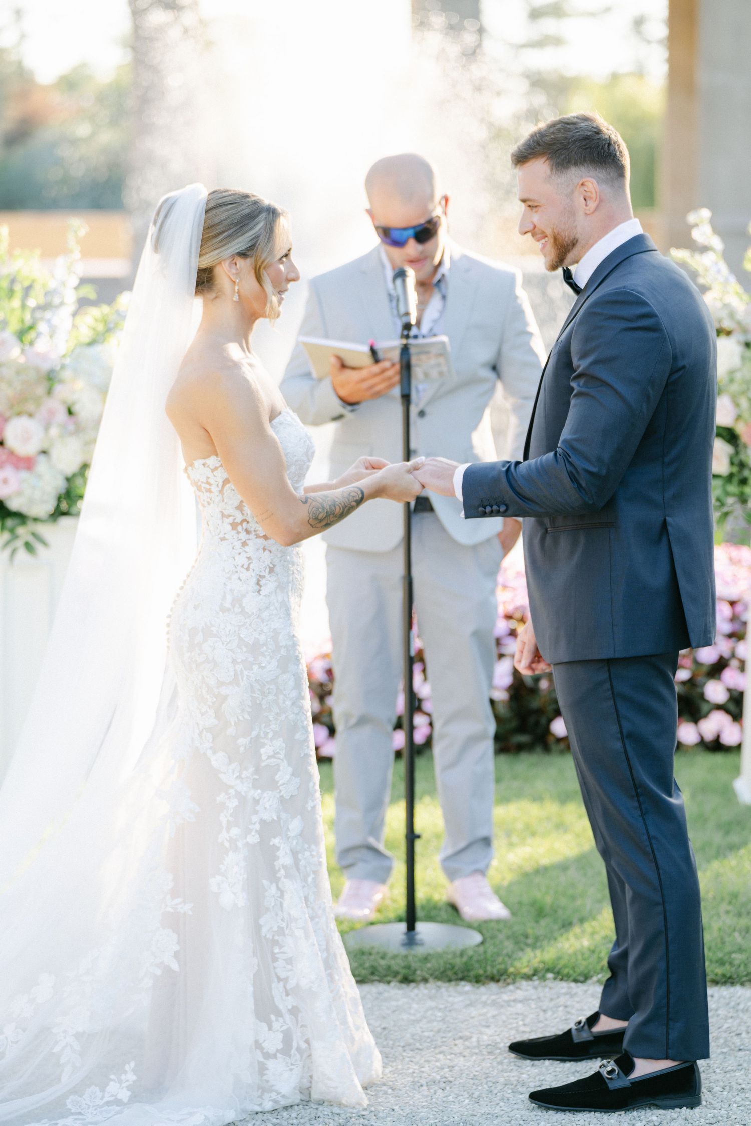 Armour House Wedding - Bride and groom exchange vows outdoors at elegant wedding ceremony with pink floral arrangements.