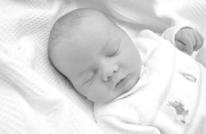 Black and white portrait of a sleeping newborn baby wrapped in a soft white blanket.