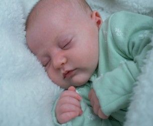 Peaceful sleeping newborn baby in mint green outfit on a fluffy white blanket.