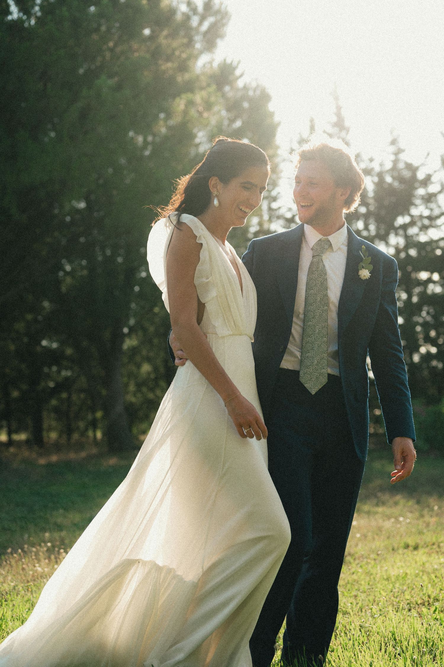Wedding couple walking through a sunlit meadow in elegant attire.