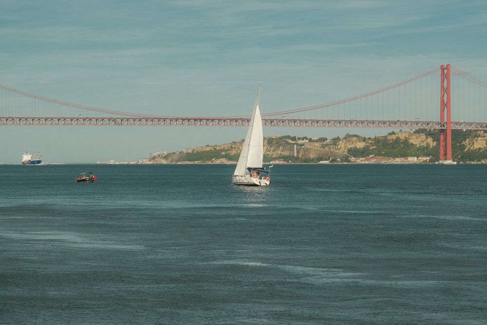Sailboat on the Tagus River with the iconic red 25 de Abril suspension bridge in the background, Lisbon, Portugal.