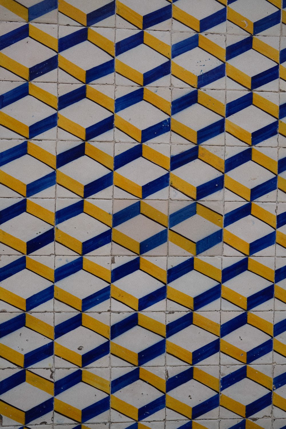 Blue, yellow, and white geometric 3D cube pattern on vintage ceramic azulejo tiles.