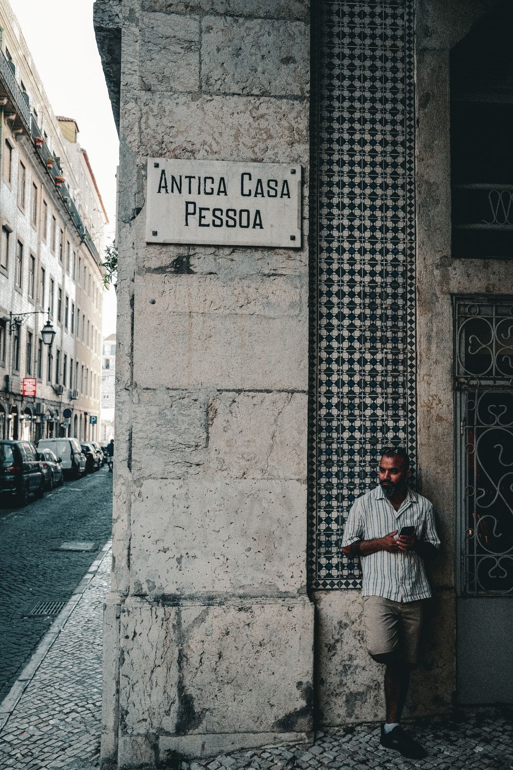 Man leaning against historic Antiga Casa Pessoa building corner with decorative tiles in Lisbon, Portugal.