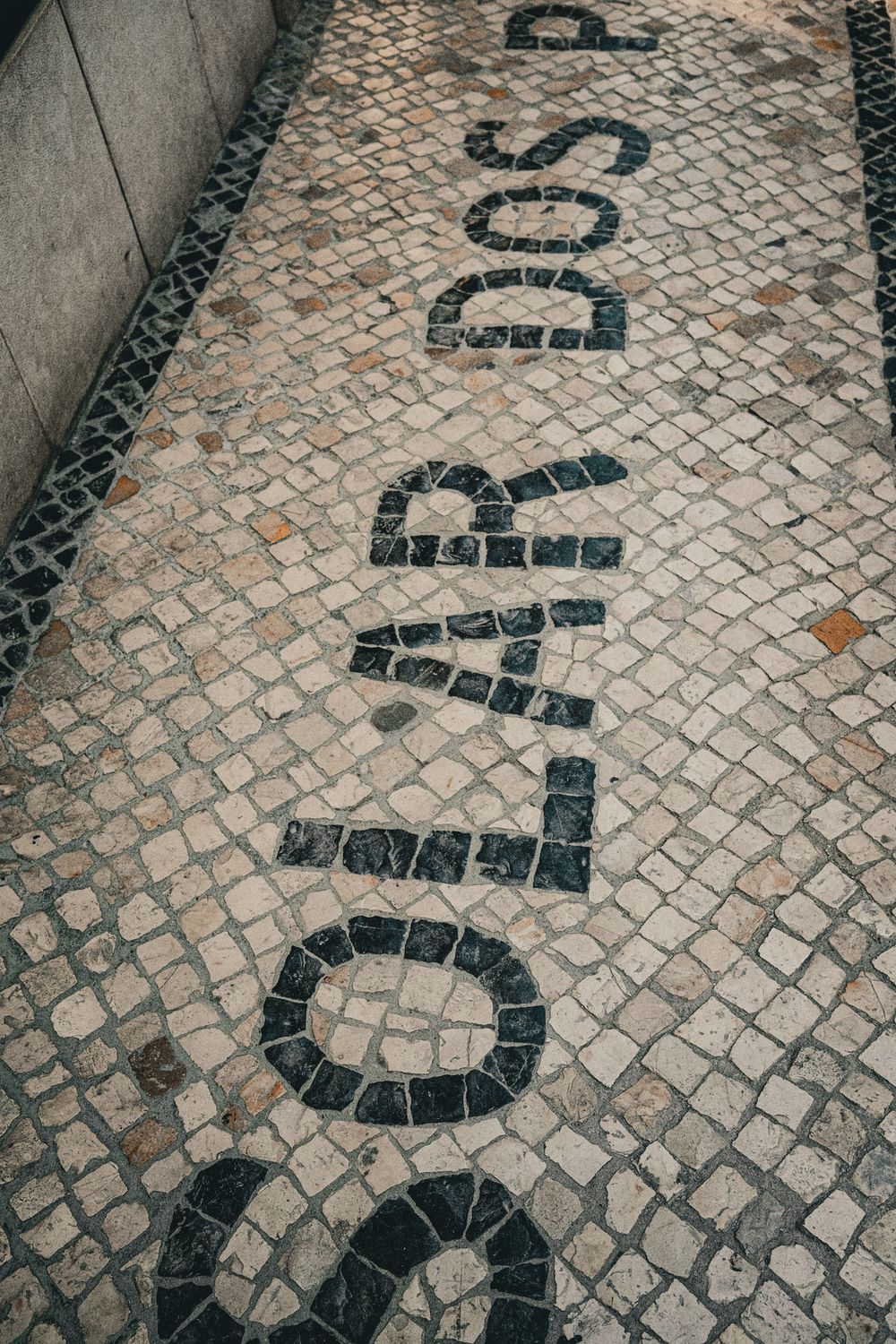 Close-up of traditional Portuguese cobblestone pavement with dark mosaic lettering spelling words on a Lisbon sidewalk.