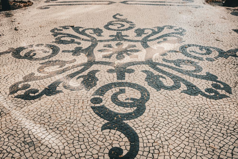 Intricate black and white mosaic cobblestone pavement with ornate floral pattern in Lisbon, Portugal.
