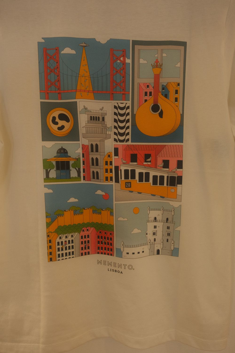 White t-shirt featuring colorful illustrated panels of Lisbon landmarks including Belem Tower, tram, and Portuguese guitar.