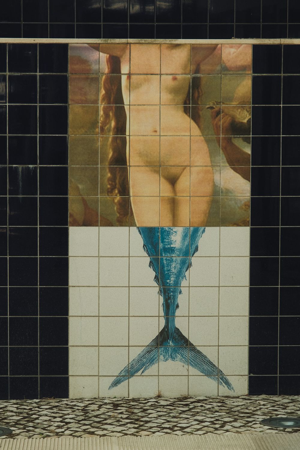 Decorative azulejo tile mural depicting a mermaid with a blue tail on a white tiled wall.
