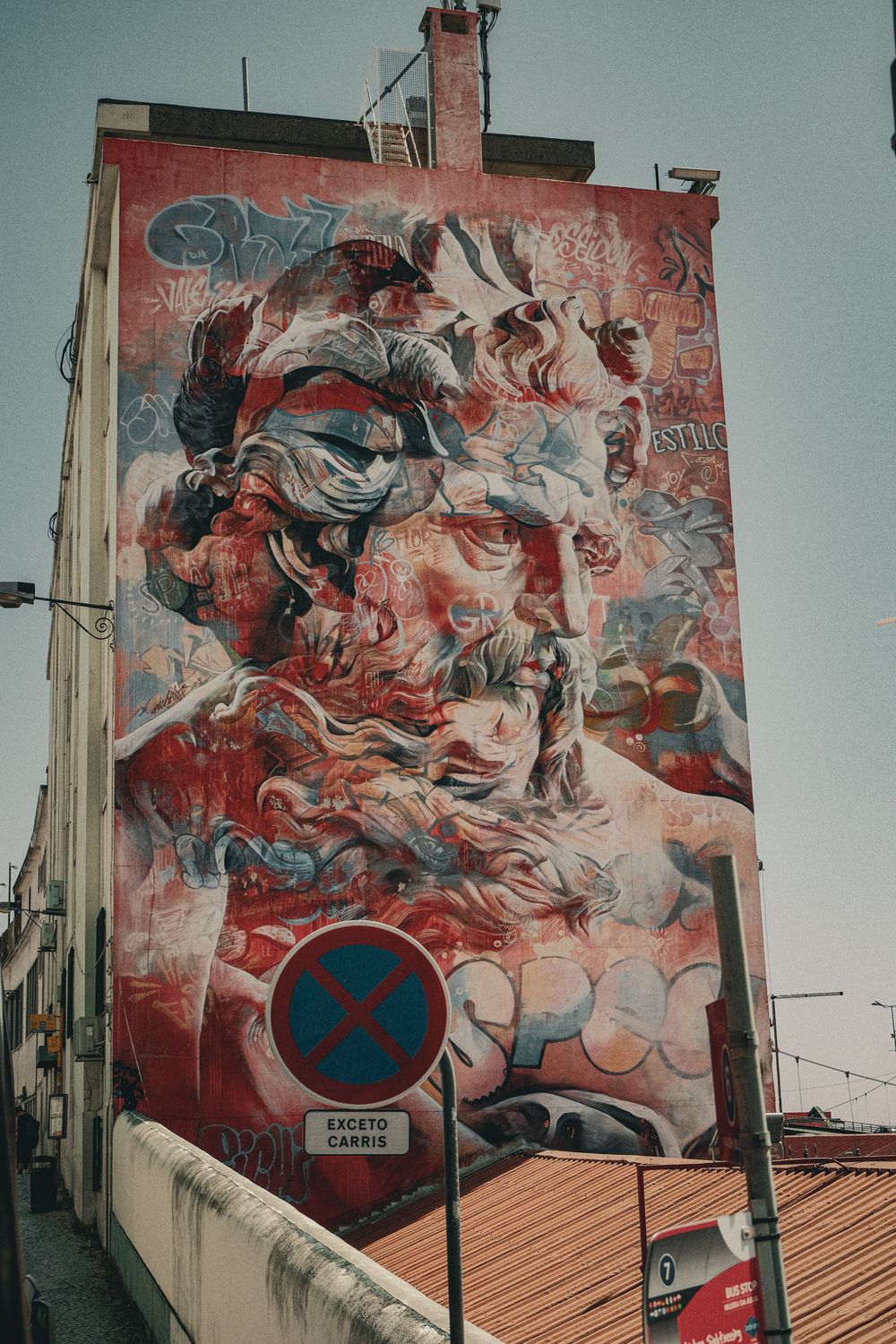 Large street art mural of a bearded man painted in red tones on a building facade in Lisbon, Portugal.