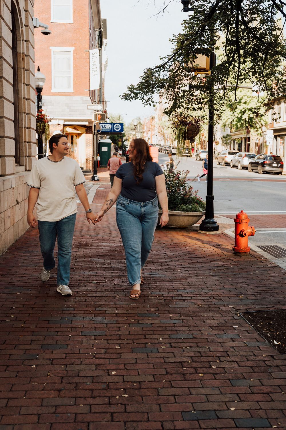 Couple holding hands walking on brick sidewalk in urban downtown area with street lamp and fire hydrant.