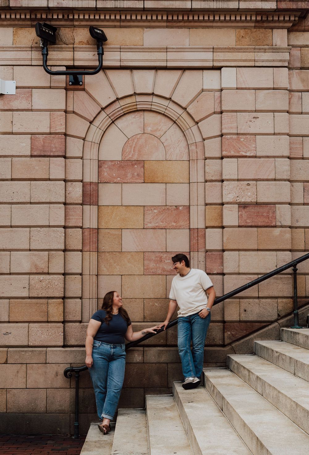 Couple holding hands on stone building steps, taking engagement photos in Downtown Lancaster in Central PA
