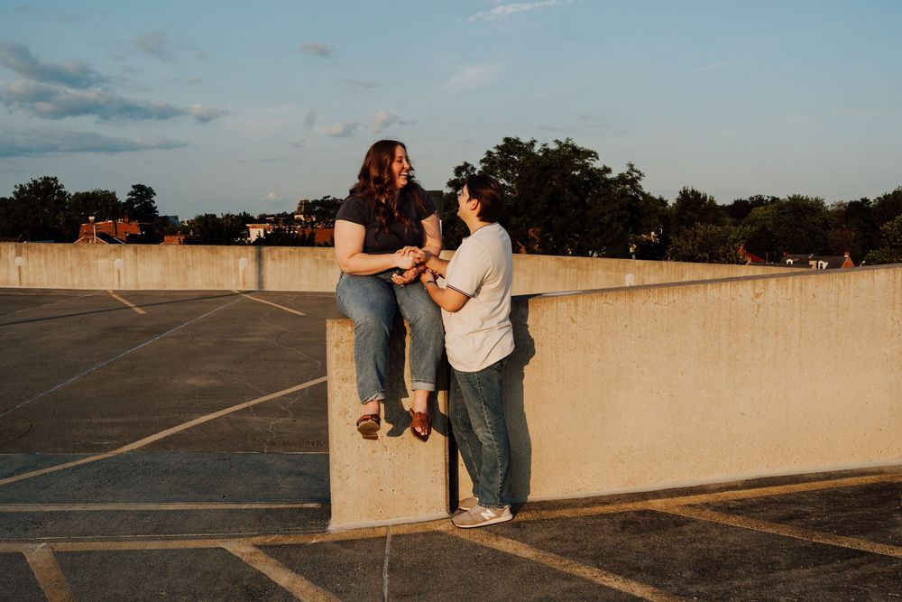 Two women share a joyful moment on a rooftop parking lot at golden hour sunset.
