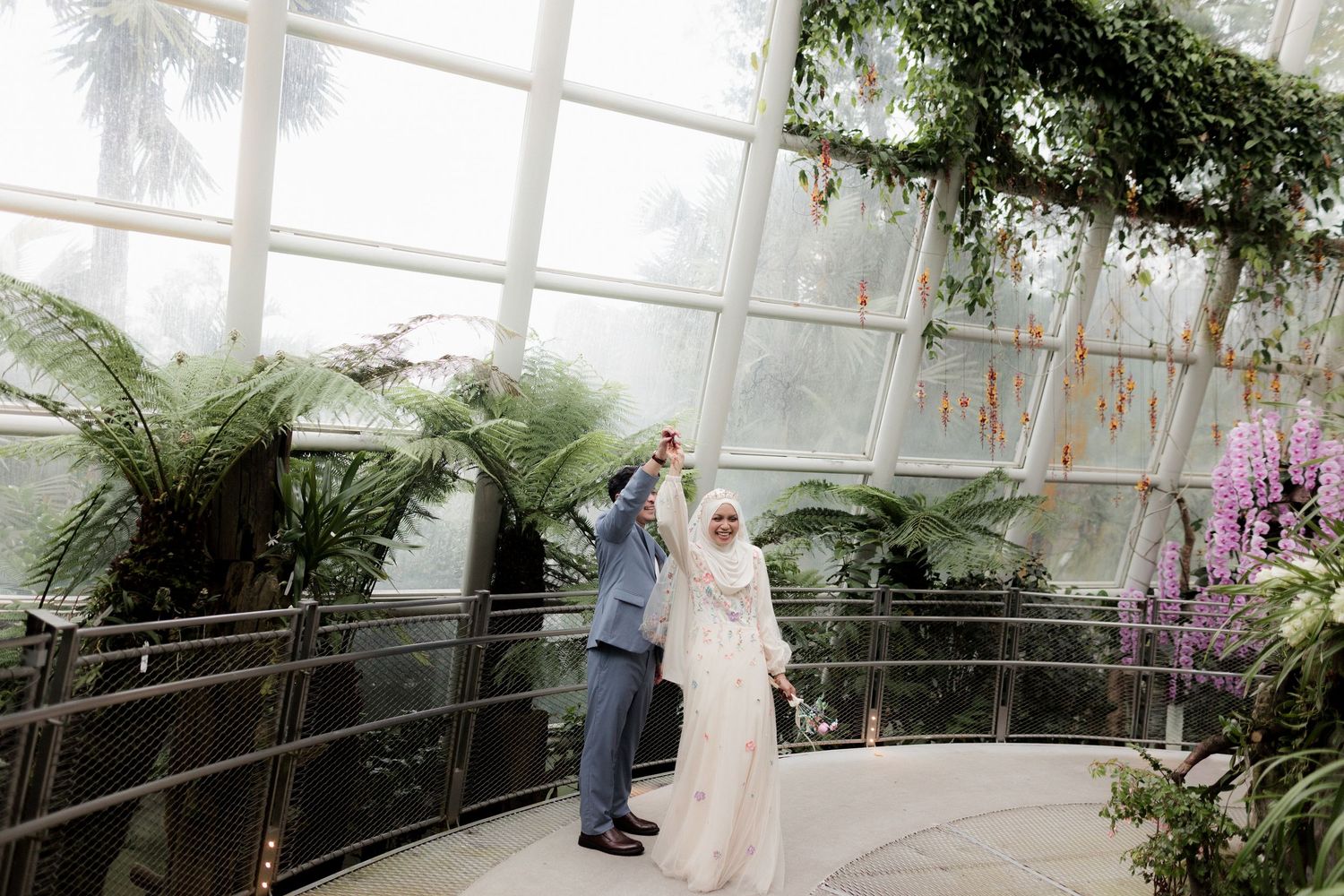 Couple dancing in a lush indoor garden atrium with tropical plants and glass ceiling.