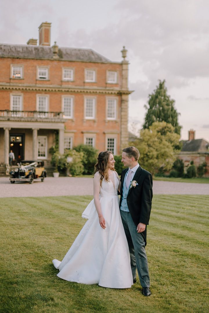 A bride and groom share a romantic moment on a lush lawn outside an elegant Georgian manor house wedding venue.