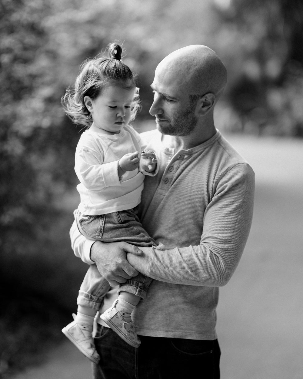 Black and white photo of a bald man tenderly holding a toddler girl outdoors.