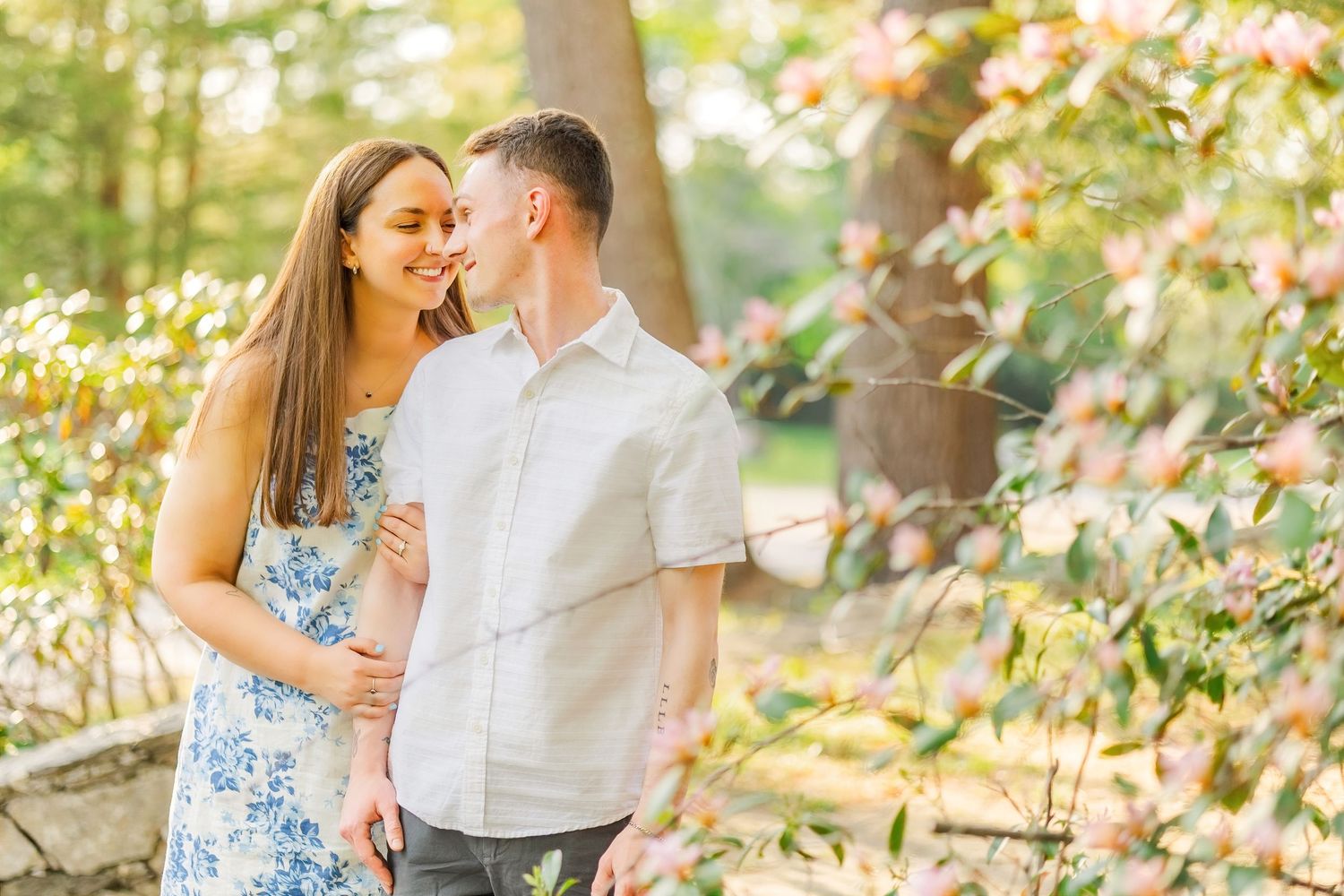 A couple shares a romantic moment surrounded by blooming spring flowers in a sunlit garden setting.