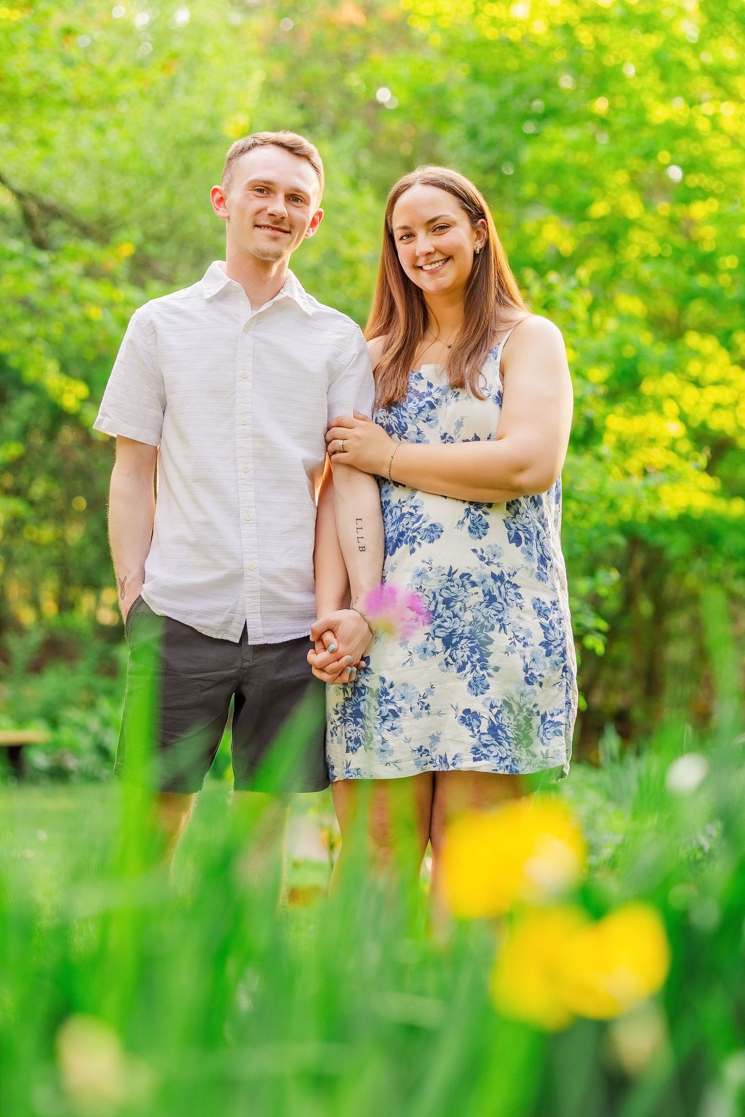 Happy couple holding hands in a lush green park surrounded by yellow tulips on a sunny day.