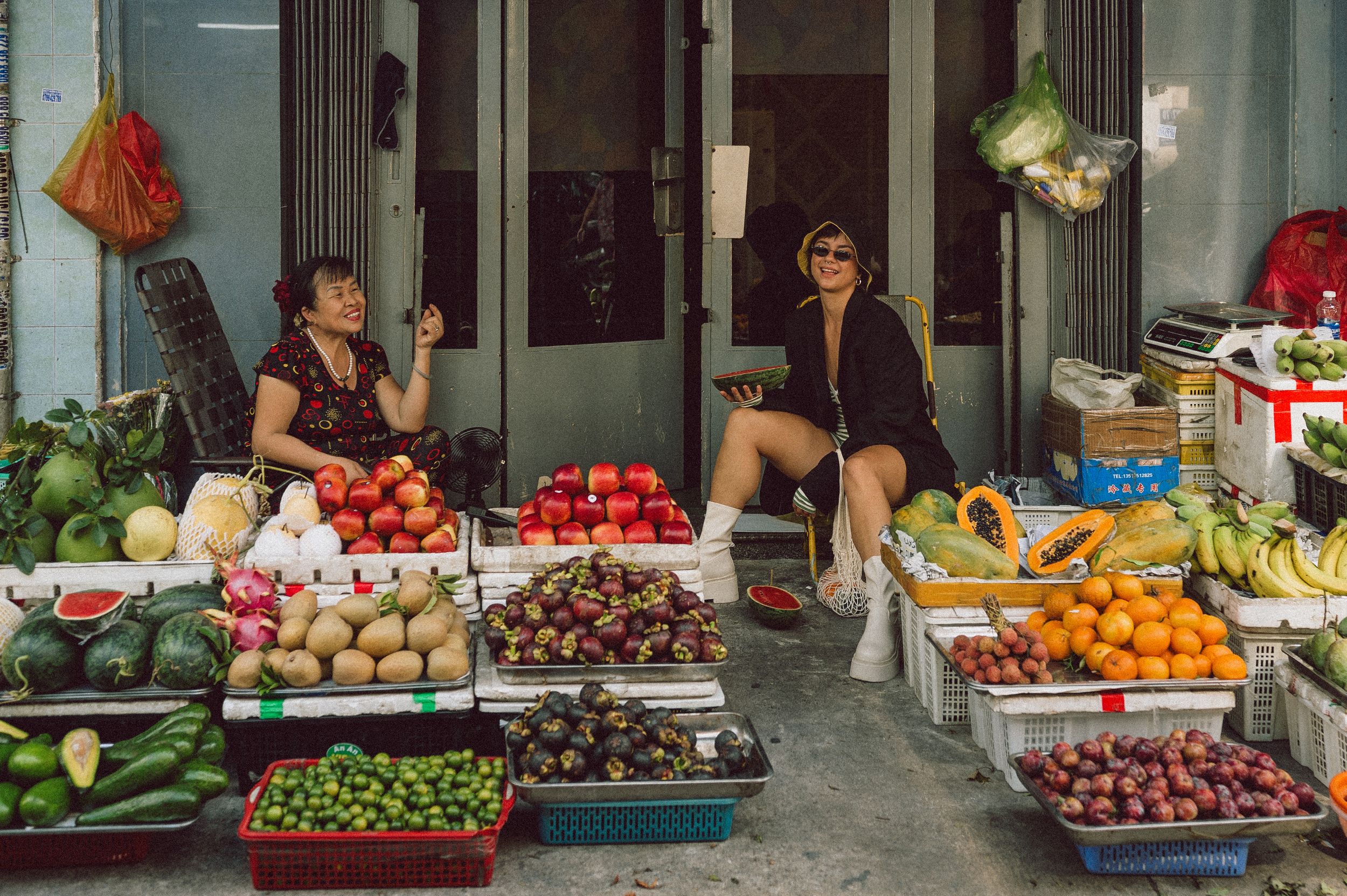 Model seated among fruit stalls at Banana Garden Market, Ho Chi Minh City — editorial lifestyle photography