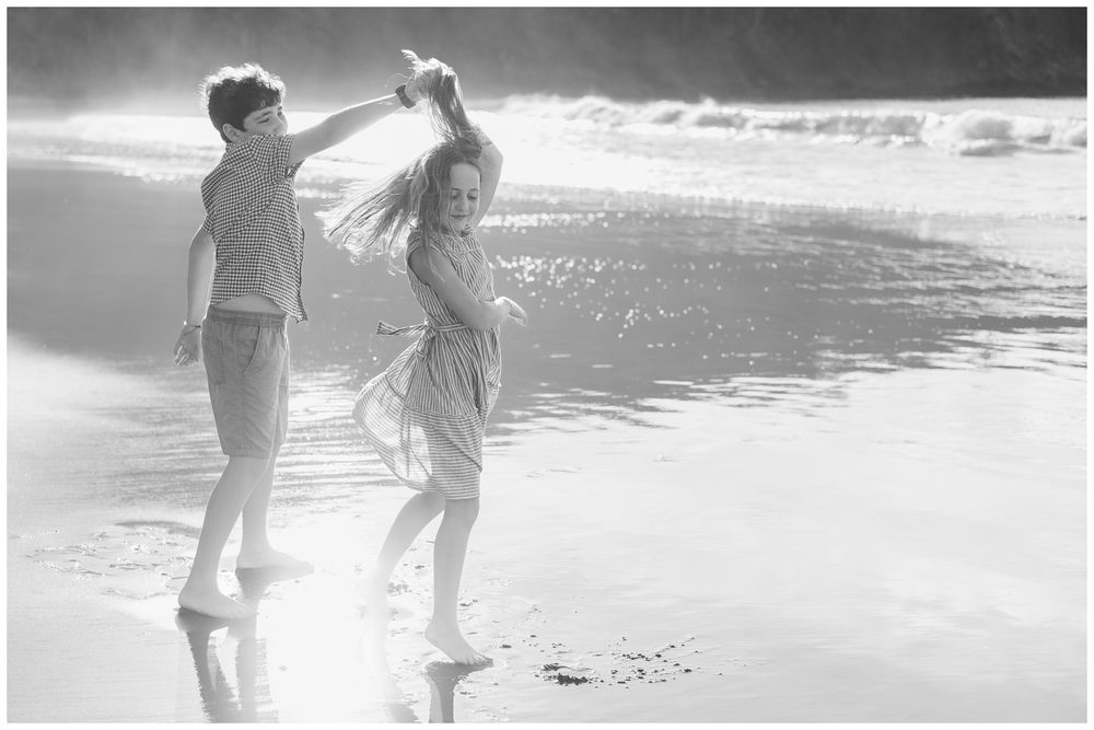Couple dancing playfully on a sandy beach shore in black and white photography.