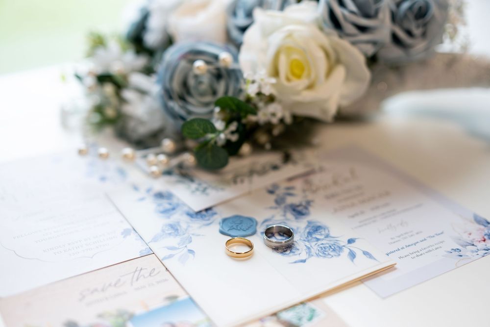 Wedding rings, blue floral invitations, and a bouquet of blue and white roses on display.