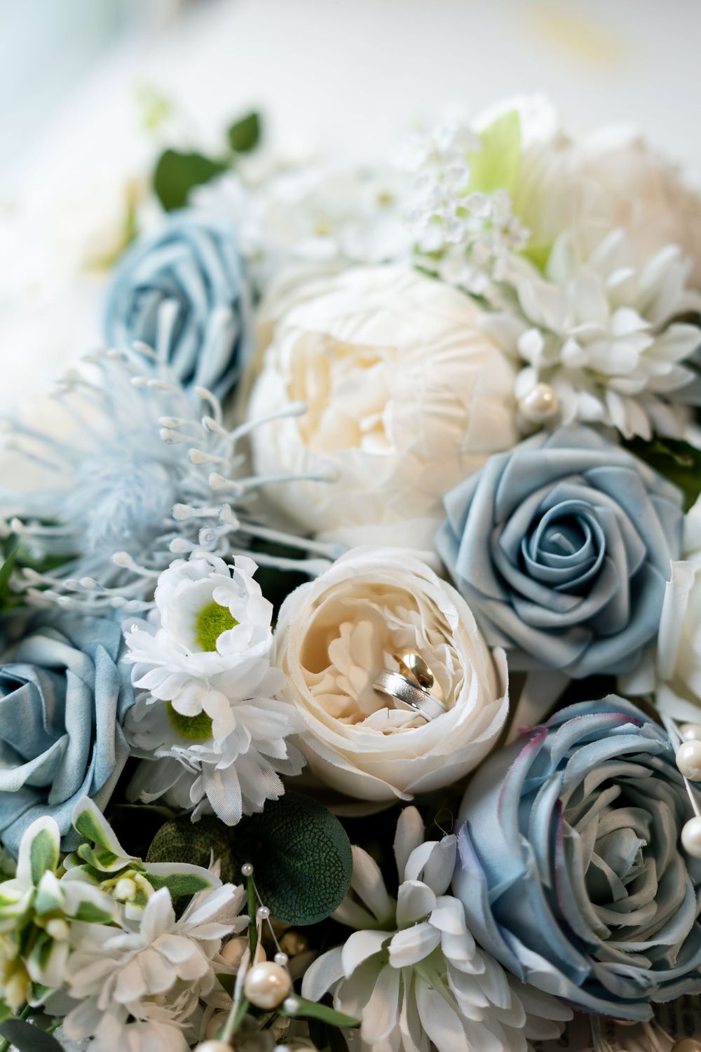 Close-up of bridal bouquet featuring blue and ivory roses with wedding rings nestled among the flowers.