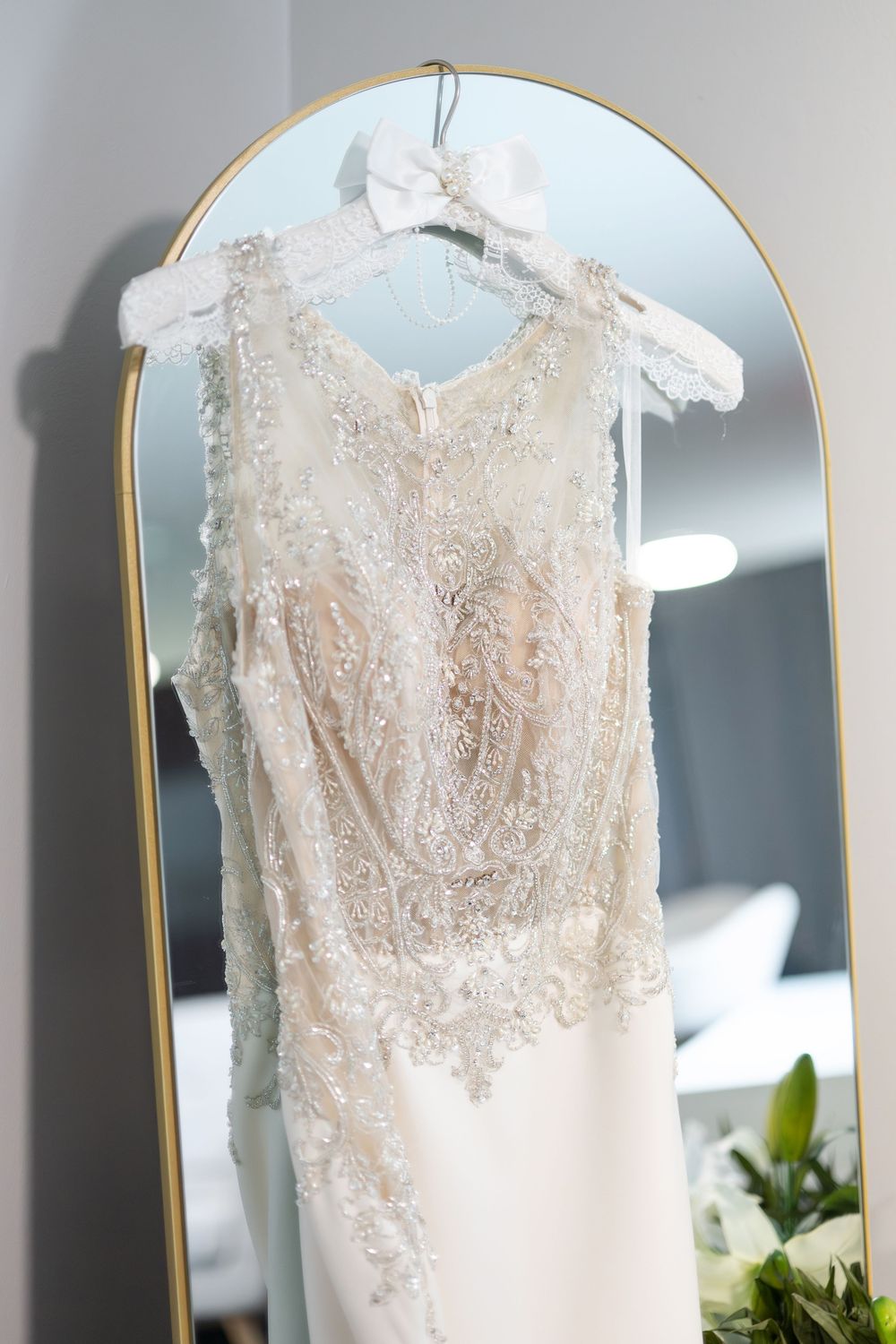 Elegant lace and beaded wedding gown hanging on a gold-framed mirror before the ceremony.