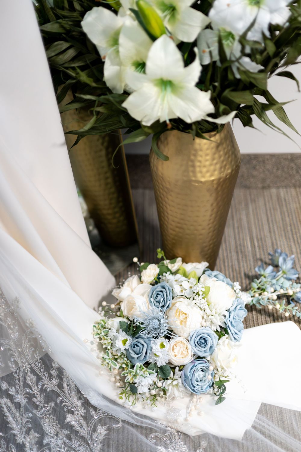 Bridal bouquet with blue and white roses resting near gold vase with white lilies.